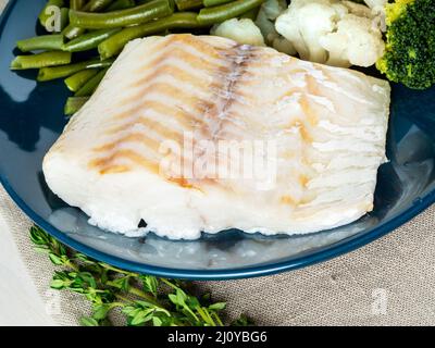 Cotto pesci di mare filetti di merluzzo con verdure sulla piastra blu, grigio igienico, vista laterale, vicino. Alimentazione sana Foto Stock