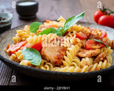 Fusilli con salsa di pomodoro, filetto di pollo con foglie di basilico Foto Stock