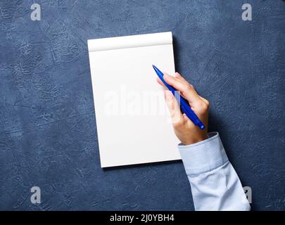 La donna scrive in taccuino su un tavolo blu scuro, mano in camicia che tiene una matita, disegno di schemchbook, vista dall'alto Foto Stock