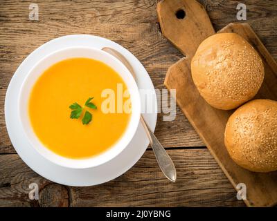 Ciotola bianca di zuppa di zucca, guarnita con prezzemolo su sfondo di legno, vista dall'alto. Foto Stock