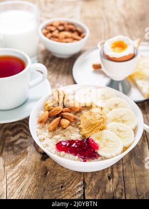 Fiocchi d'avena con noci e marmellata, uova bollite morbide, fuoco selettivo, vista laterale, cornice verticale Foto Stock