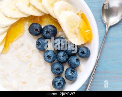 Farina d'avena con banane, mirtilli, chia, marmellata, miele su sfondo blu di legno. Colazione sana. Vista dall'alto, primo piano Foto Stock