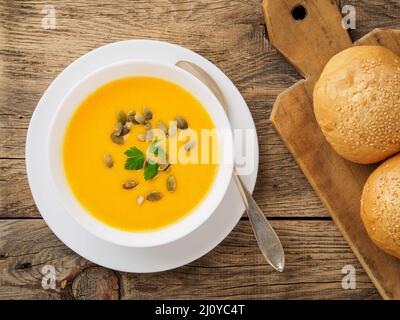 Ciotola bianca di zuppa di zucca, guarnita con prezzemolo e semi di girasole su sfondo di legno Foto Stock