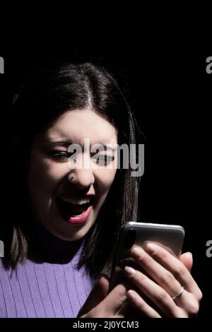 donna che guarda il mobile con un'espressione di disgusto su sfondo nero Foto Stock