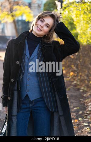 Giovane donna bionda dai capelli corti in giacca a righe, jeans e gilet tocca i capelli Foto Stock