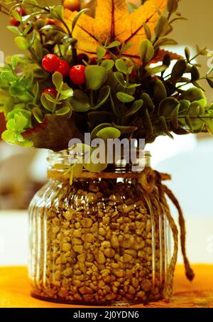 Colpo verticale delle foglie di bacche artificiali in un vaso di vetro pieno di piccole pietre Foto Stock