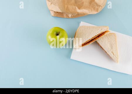 Vista ad angolo alto della mela verde con burro di arachidi e sandwich gelatina da sacchetto di carta sul tavolo Foto Stock