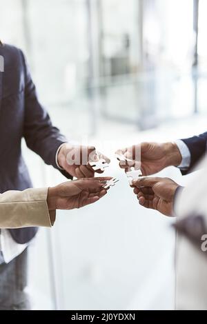 Sulla base della loro visione collettiva. Primo piano di un gruppo di uomini d'affari irriconoscibili che uniscono i pezzi di puzzle in un ufficio. Foto Stock