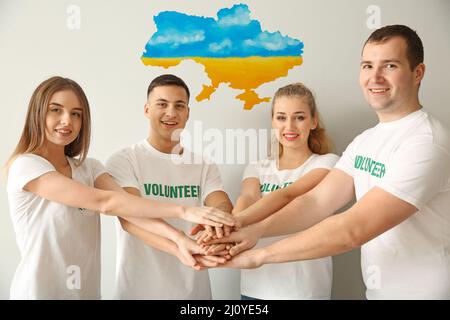 Gruppo di volontari che mettono le mani insieme e mappa dell'Ucraina su sfondo chiaro. Assistenza umanitaria ai rifugiati Foto Stock