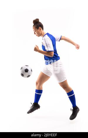 Vista laterale del giovane femminile biraciale in pallina da calcio a mezz'aria mentre gioca a calcio Foto Stock