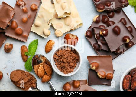 Pezzi di gustoso cioccolato con noci e cacao in polvere su sfondo colorato Foto Stock