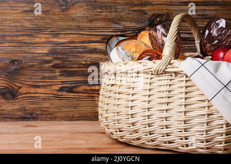 Cestino di vimini con cibo gustoso per picnic su sfondo di legno Foto Stock