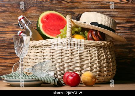 Cestino di vimini con cibo gustoso, bevanda per picnic e stoviglie su sfondo di legno Foto Stock