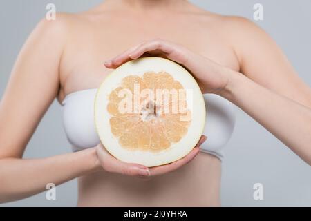 vista croppata della donna con metà del pompelmo maturo isolato sul grigio Foto Stock