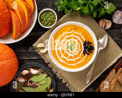 Cibo divertente per Halloween. Zuppa di purea di zucca, ragnatela, vecchio tavolo di legno scuro, vista dall'alto. Foto Stock