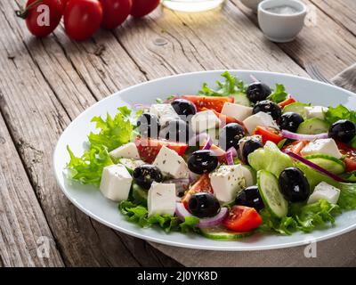 Insalata greca su piatto bianco su vecchio tavolo rustico in legno, vista laterale Foto Stock