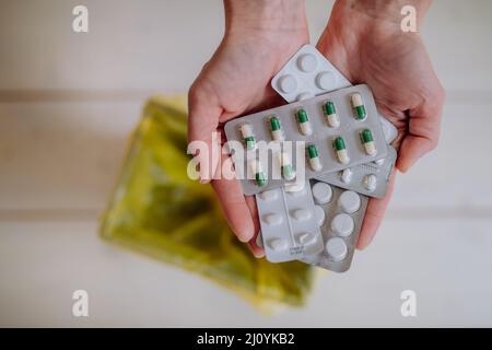 Le mani della donna tengono e gettano pillole scadute al cestino. Foto Stock