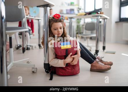Piccola ragazza Ucraina triste seduta sul pavimento a scuola, concetto di iscrizione dei capretti ucraini alle scuole. Foto Stock