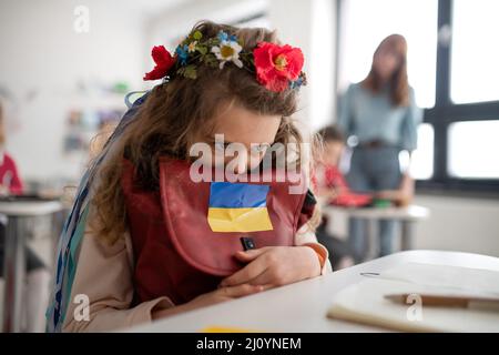 Piccola ragazza Ucraina triste seduta a scuola, concetto di iscrizione dei bambini ucraini alle scuole. Foto Stock