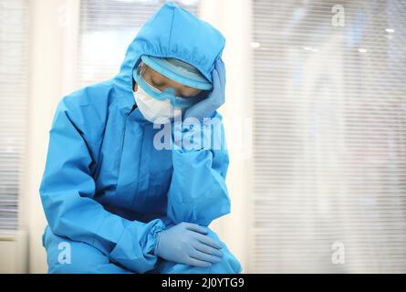 Tired depressed nurse in personal protective equipment PPE after difficult shift during Covid-19. Stock Photo