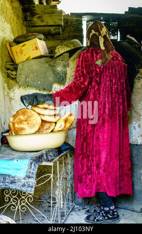 Una donna di villaggio sta cuocendo il pane tagico tradizionale, non o naan ad un villaggio remoto in Tagikistan Foto Stock