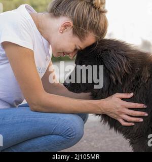 Vista laterale donna con morbido cane nero all'aperto Foto Stock