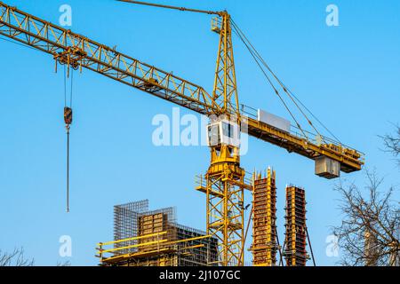 Gru a torre gialla. Gru girevole ad alta quota su sfondo di cielo blu e corone di alberi Foto Stock