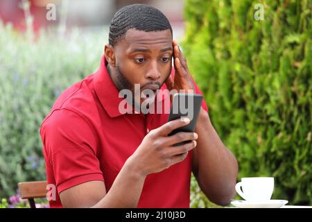 Uomo stupito con la pelle nera che controlla il contenuto del telefono cellulare in un bar Foto Stock