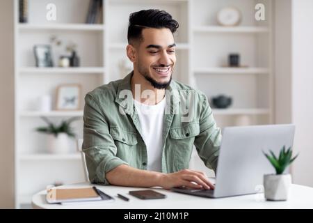 Telelavoro. Happy Young Arab Man che lavora da remoto con il notebook presso l'ufficio domestico Foto Stock