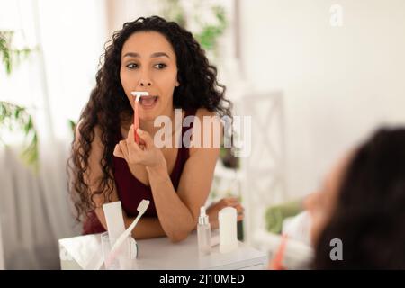 Bella giovane donna brunette rasando il labbro superiore, rimuovendo baffi indesiderati davanti allo specchio a casa, spazio vuoto Foto Stock