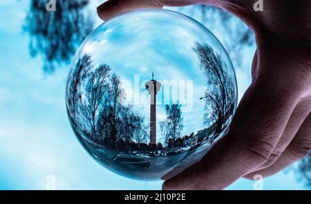 Primo piano di una mano che tiene una lente palla che riflette un edificio e il cielo Foto Stock