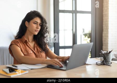 Focalizzata giovane freelance femminile che lavora online, utilizzando il computer portatile a casa, spazio copia Foto Stock