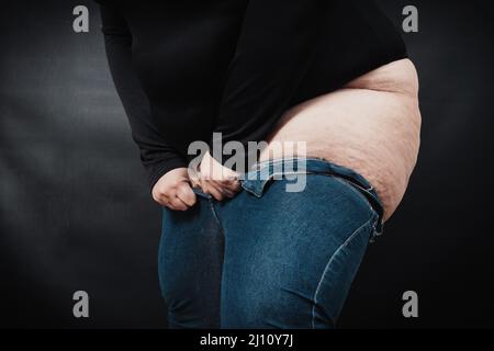 donna grassa che tira i jeans su se stessa su uno sfondo nero Foto Stock