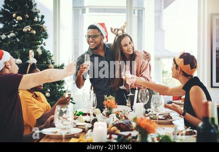 Grazie al vostro primo pranzo di Natale insieme. Scatto corto di una giovane coppia allegra tostatura con i loro amici mentre si ha pranzo di Natale a. Foto Stock