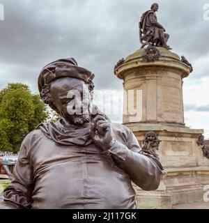 Una statua grinnesca del personaggio comico di William Shakespeare Falstaff si erge davanti a una statua del Bard stesso al monumento Gower, Stratford, Regno Unito. Foto Stock