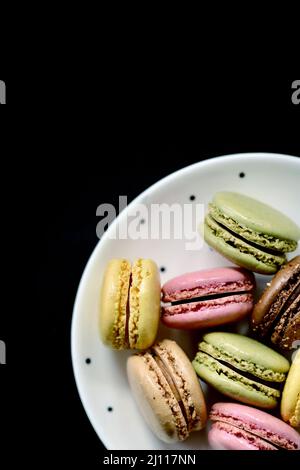 Un piatto di lamponi, caramello, limone e pistacchio macaron su sfondo nero Foto Stock