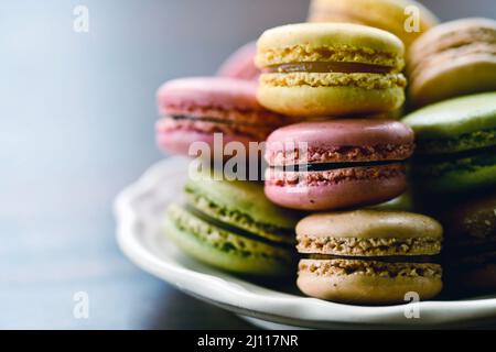 Un mucchio di biscotti francesi di macaron accatastati su un piatto su un tavolo di legno in luce naturale Foto Stock