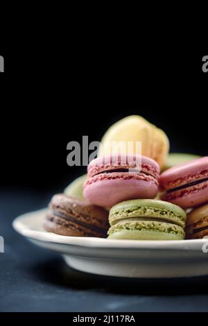 Mucchio di biscotti al lampone, pistacchio, cioccolato e limone macaron su un piatto con fondo nero. Foto Stock