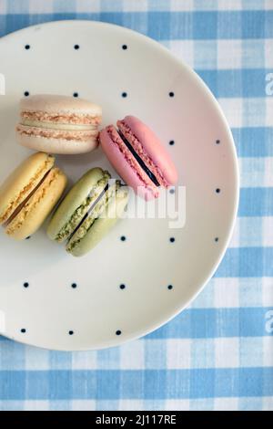 Quattro biscotti francesi di macaron su un piatto punteggiato di polka su un panno da tavolo a scacchi blu e bianco Foto Stock