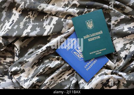 Documento d'identità militare ucraino e passaporto straniero su tessuto con tessuto di camouflage pixellato. Panno con motivo camo in pixel grigio, marrone e verde Foto Stock