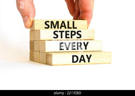 Simbolo piccoli passi ogni giorno. Parole di concetto piccoli passi ogni giorno su blocchi di legno. Mano dell'uomo d'affari. Bella tabella bianca sfondo bianco. St. Piccola Foto Stock