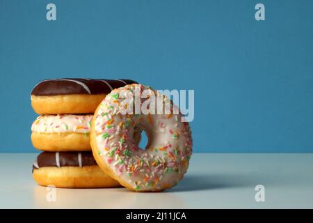 Una bella torretta di tre deliziose ciambelle fresche con diversi colori spolverini e cioccolato. Una ciambella si trova lateralmente. Foto Stock