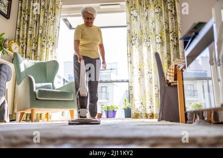 Donna anziana che usa l'aspirapolvere per pulire la casa Foto Stock