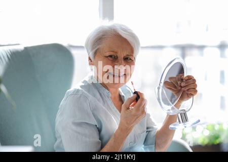 Donna anziana che fa il trucco di fronte allo specchio Foto Stock