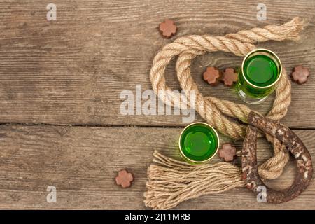 Concetto di giorno di San Patrizio. Cocktail verde tradizionale, cioccolato dolce a forma di foglie di trifoglio, ferro di cavallo, corda d'epoca. Festa tradizionale dicembre Foto Stock