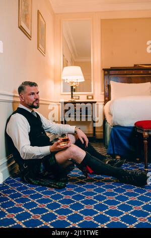 bell'uomo coraggioso e maturo scotsman in kilt che beve whiskey sul pavimento in una lussuosa camera d'albergo. Stile, moda, stile di vita, cultura, viaggi, Foto Stock