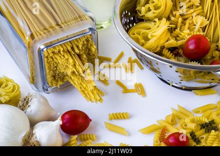 Gruppo di pasta cruda con verdure in un setaccio in acciaio inox sulla superficie bianca Foto Stock