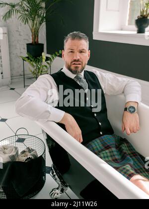 bell'uomo coraggioso e maturo scotsman in forno e vestito posato in bagno. Stile, lavoro da casa, moda, stile di vita, blocco, cultura, Foto Stock