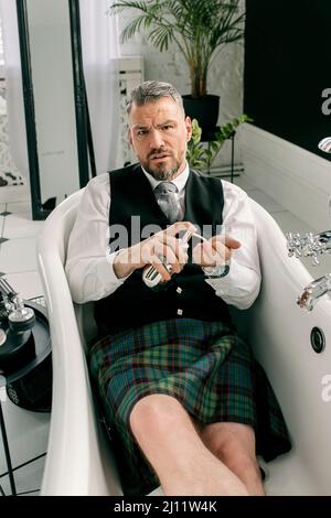 bell'uomo coraggioso e maturo scotsman in forno e vestito posato in bagno. Stile, lavoro da casa, moda, stile di vita, blocco, cultura, Foto Stock