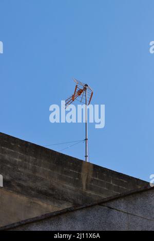 Immagine di un'antenna per ricevere il segnale televisivo digitale terrestre sulla parte superiore di un edificio con il cielo blu sullo sfondo Foto Stock